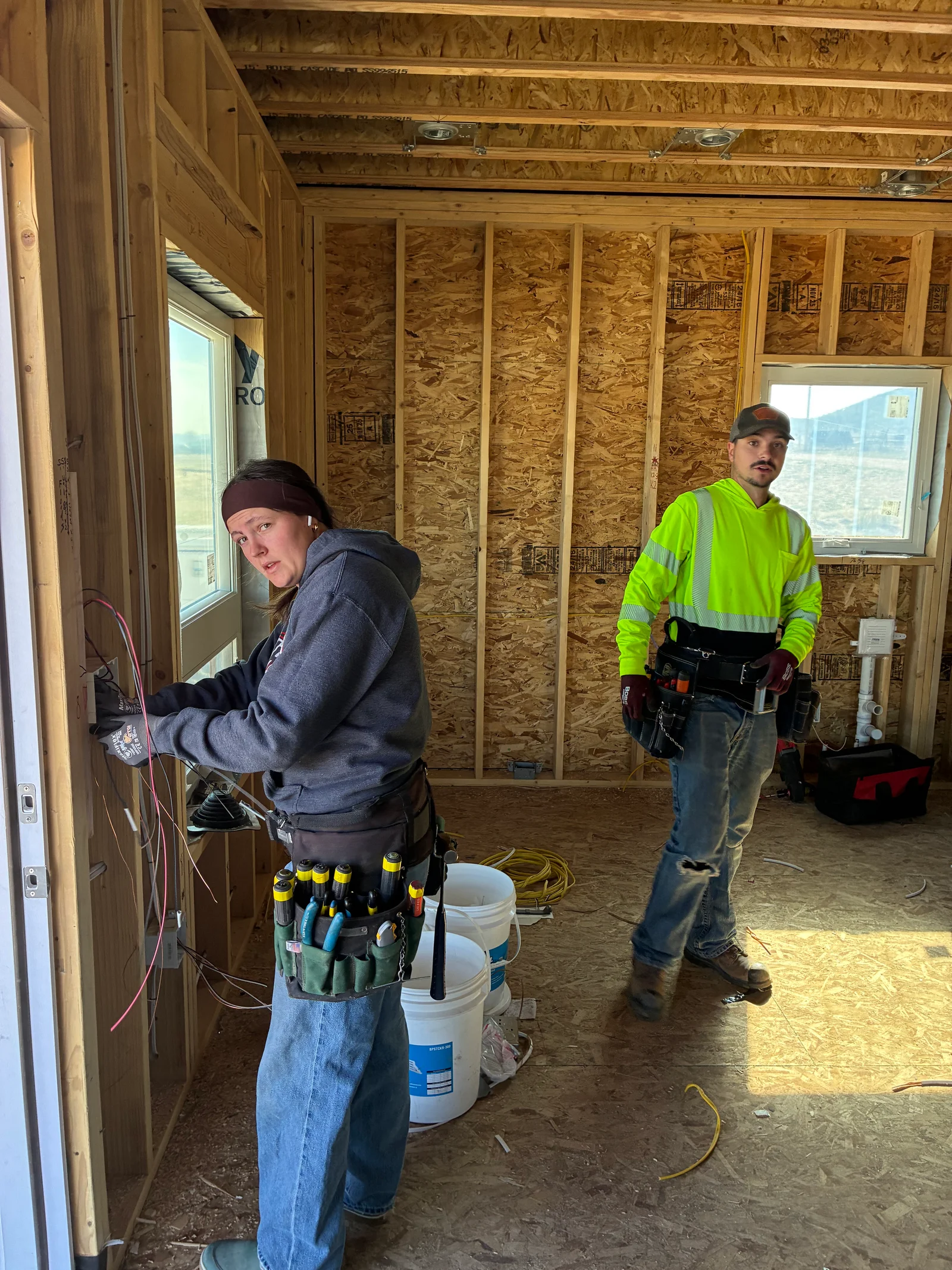 An electrician running new wiring through open wall framing during a home remodel in Westcliffe, Colorado. Rough-in electrical work visible before drywall installation in a rural mountain home.