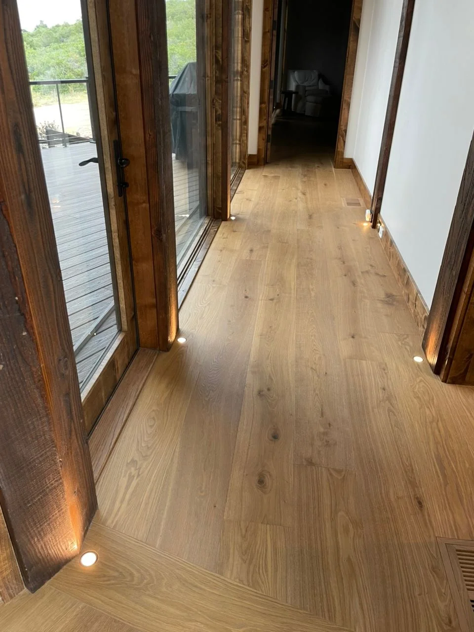 A residential living room in a Westcliffe, Colorado home with newly installed recessed ceiling lights and a central pendant fixture illuminating a mountain-view interior. An electrician from LakeFork Electric LLC completes the final fixture connection from a ladder.