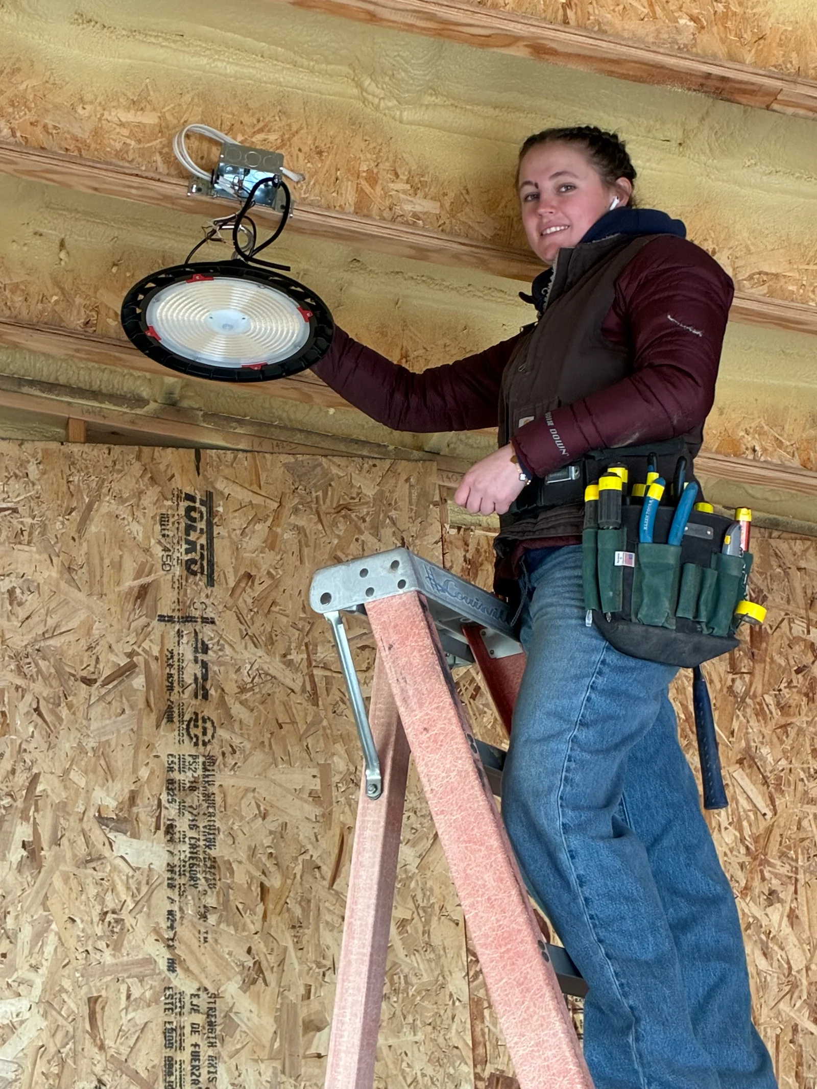 Kate Doughty, Residential Wireman at LakeFork Electric LLC, installing a light fixture on a ladder